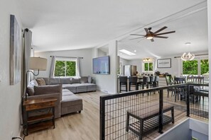 A spacious living area with a grey sectional sofa, a wooden coffee table, and a dining area with a glass table and chairs. - Arbor House - A House for Families & Friends (Lyndon Station)