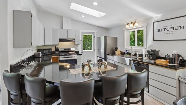 A modern kitchen with a central island, stainless steel appliances, and a dining area with chairs. - Arbor House - A House for Families & Friends (Lyndon Station)