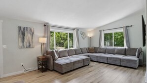 A modern living room with a sectional sofa, a floor lamp, and large windows. - Arbor House - A House for Families & Friends (Lyndon Station)