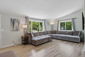 A modern living room with a sectional sofa, a floor lamp, and large windows. - Arbor House - A House for Families & Friends (Lyndon Station)