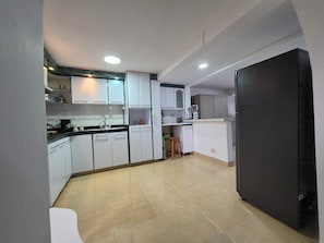 Een kleine keuken met witte kasten, een zwarte koelkast en een betegelde vloer.