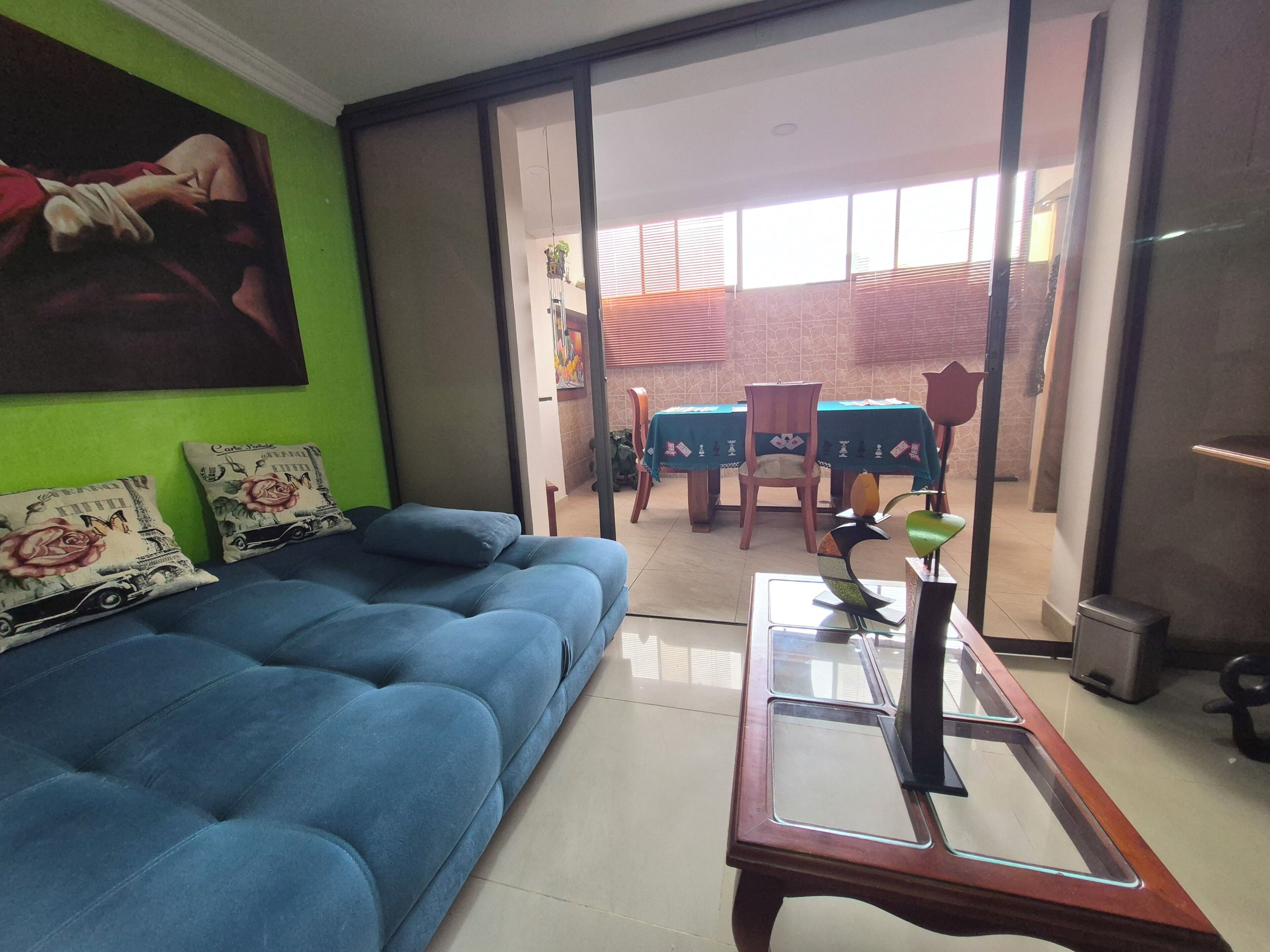 A living room with a blue sofa, a glass coffee table, and a painting on the wall.