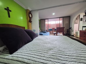 Een slaapkamer met een groot bed, een houten kruis aan de muur en uitzicht buiten door een schuifdeur.