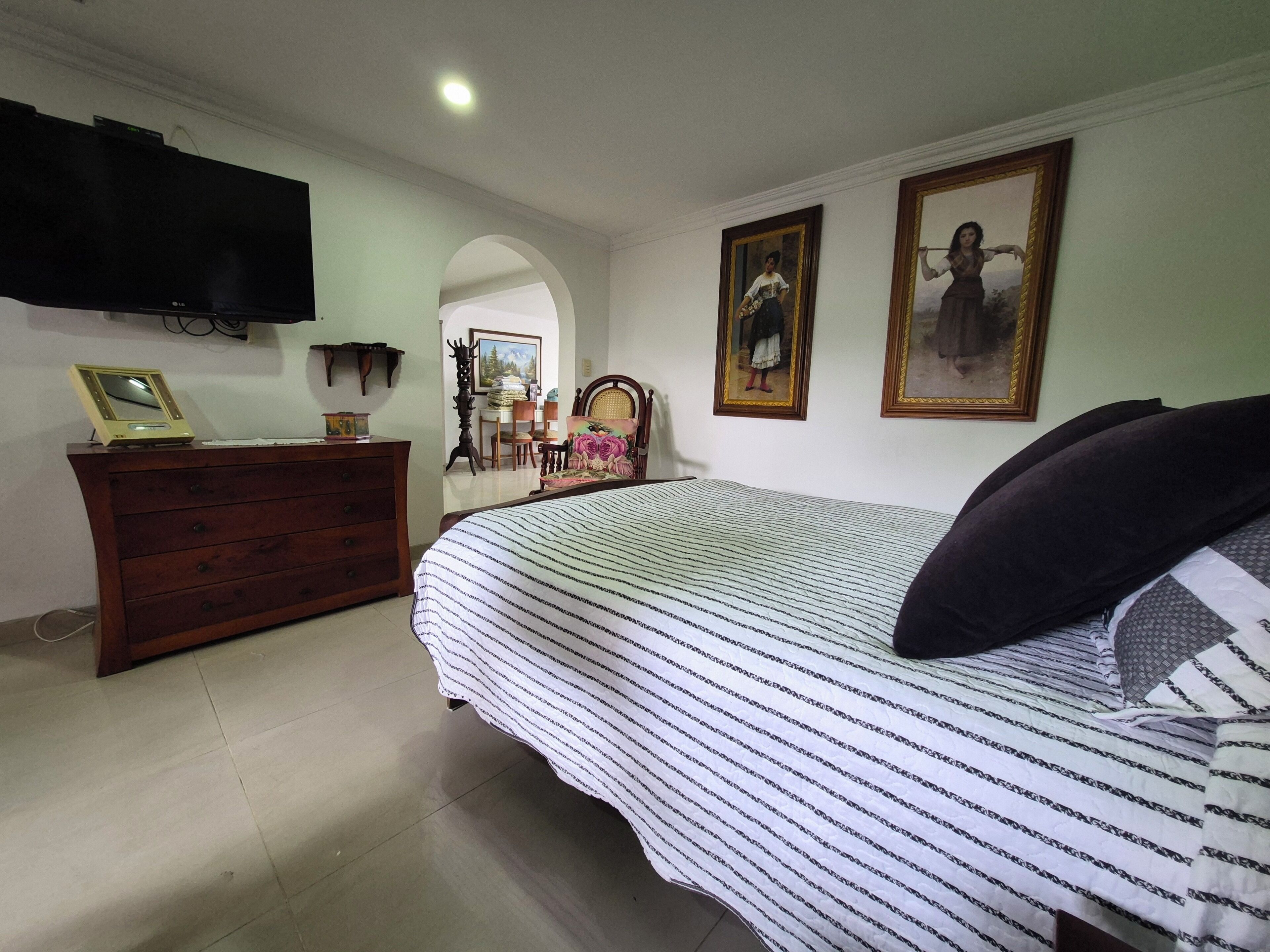 A bedroom with a bed, dresser, TV, and paintings on the wall.