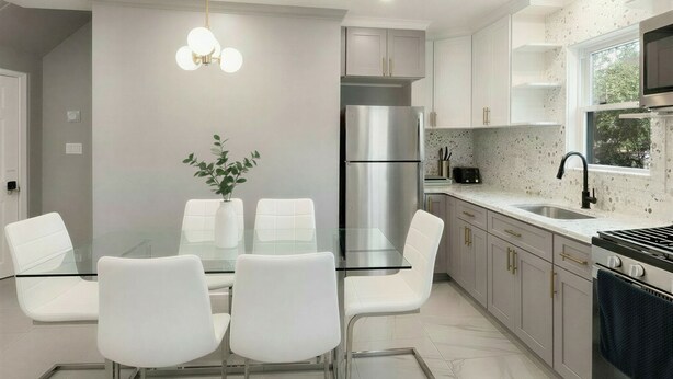 A modern kitchen with a stainless steel refrigerator, a microwave, and a gas stove. There is a dining area with a glass table and white chairs.