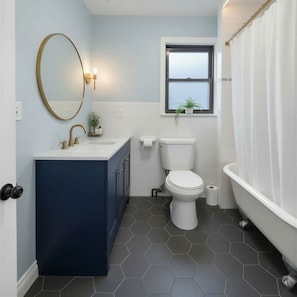 A bathroom with a dark blue vanity, a white toilet, a window with a plant, and a white bathtub.
