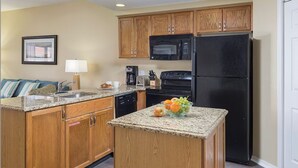 A kitchen with wooden cabinets, a black refrigerator, a microwave, a dishwasher, and a granite countertop. - Relaxing Branson Getaway with Pools & Spacious 2BR Vacation Suite (Branson)