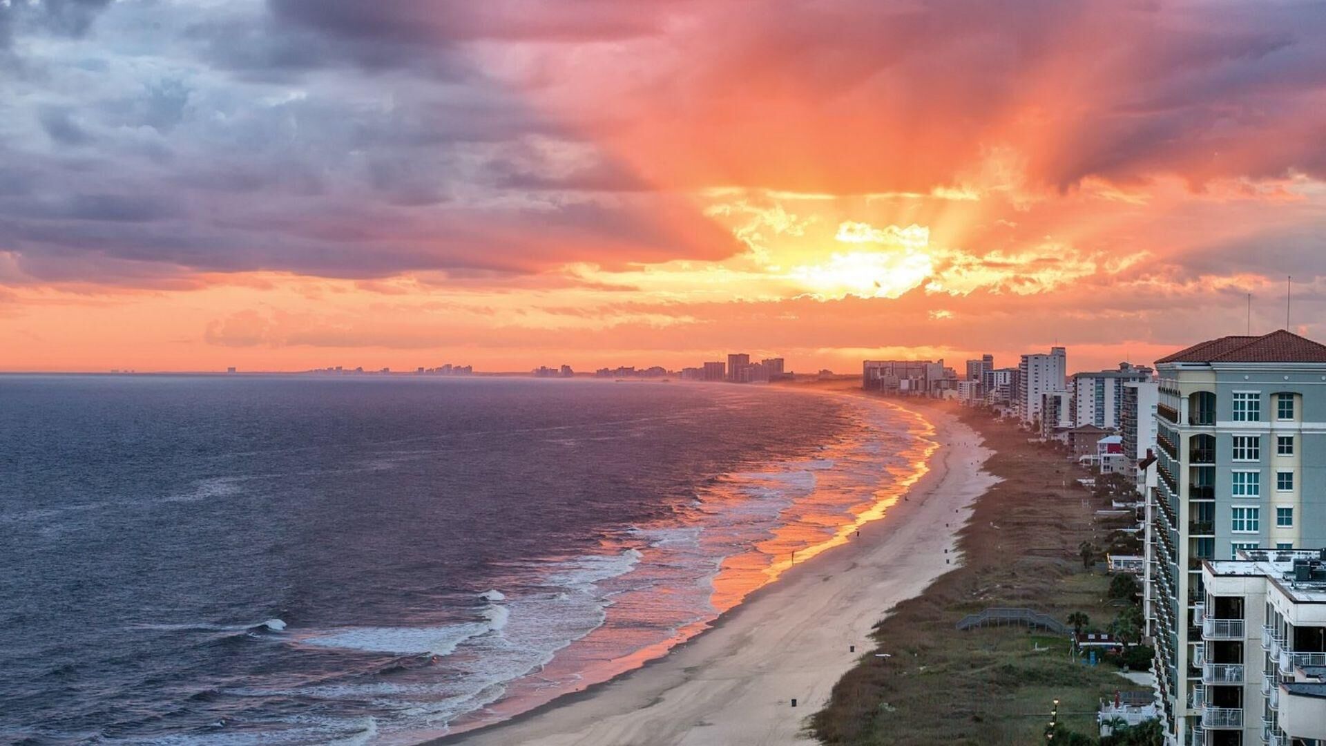 A coastal cityscape with a beach and high-rise buildings during sunset.