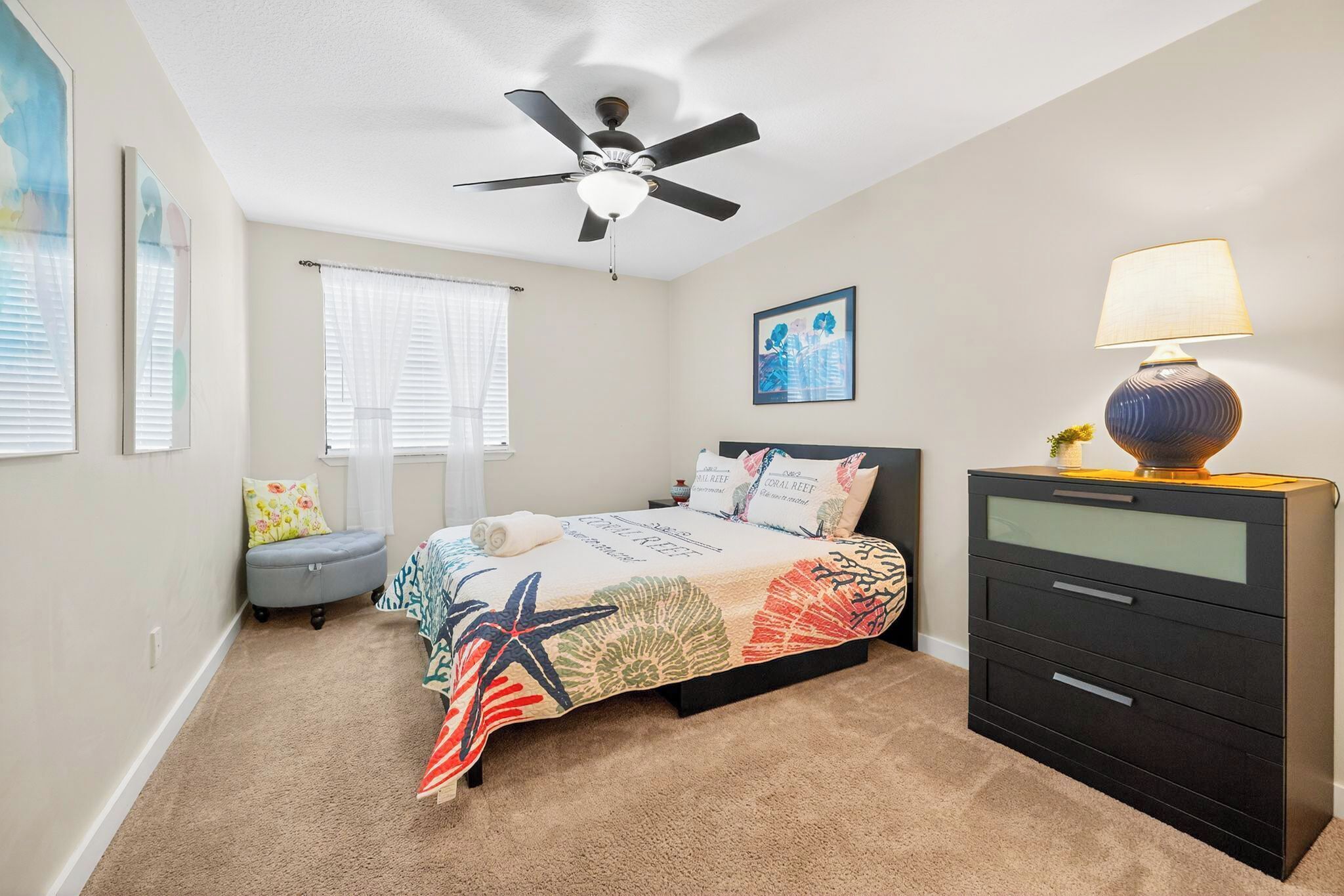 A bedroom with a bed, a ceiling fan, a nightstand, a lamp, and a dresser.