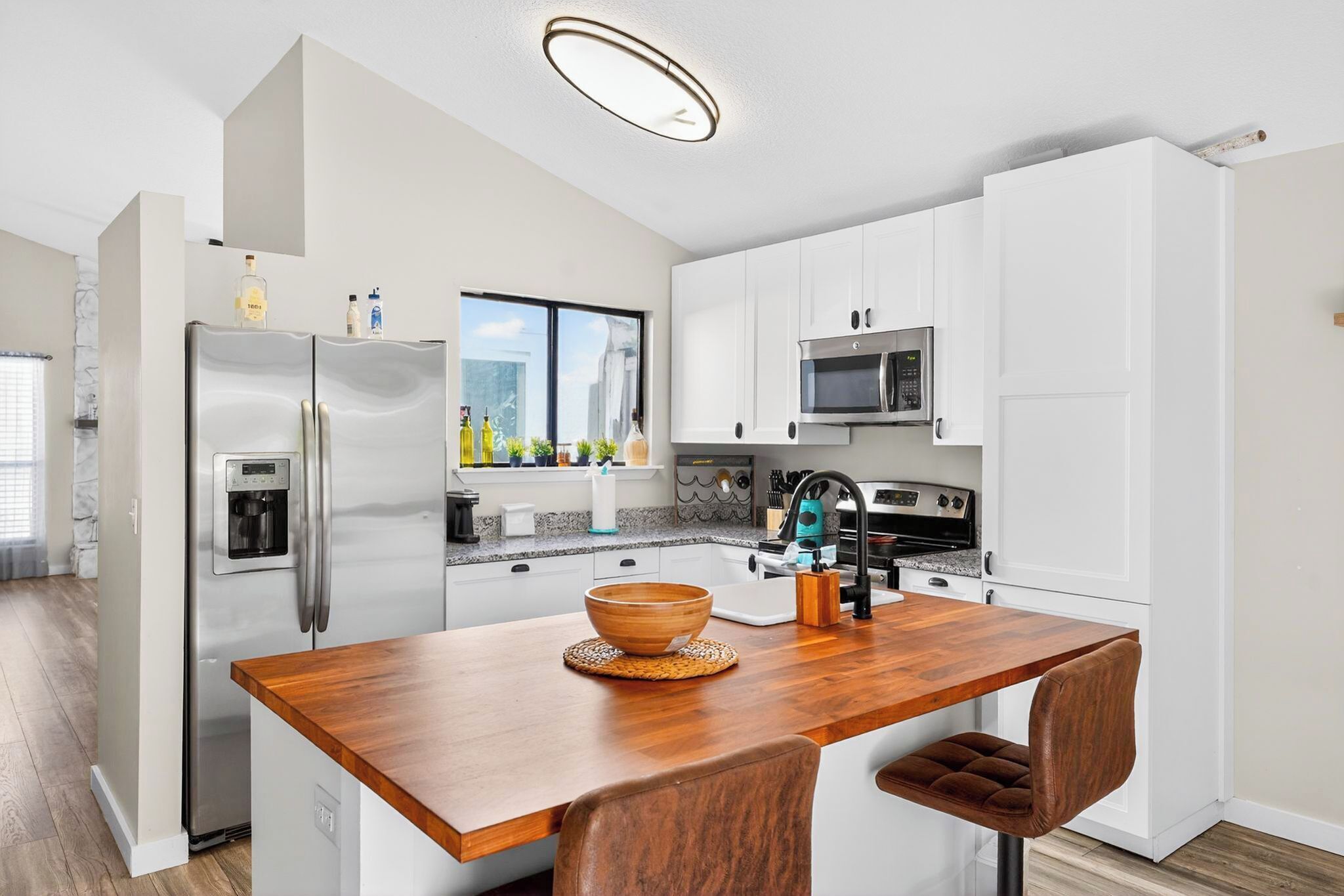 A modern kitchen with white cabinets, stainless steel appliances, a wooden island, and a view of the city.