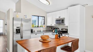 A modern kitchen with white cabinets, stainless steel appliances, a wooden island, and a view of the city.