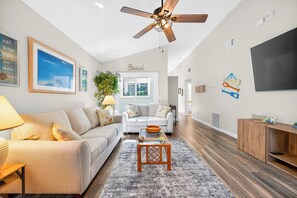 Ein Wohnzimmer mit Deckenventilator, einer Couch, einem Couchtisch und einem Fernseher.