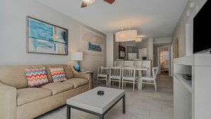 A living room with a sofa, a coffee table, a dining area with chairs, a kitchen, and a TV. - Family Beach Vacation with Pools & Spacious 2BR Coastal Resort Stay (North Myrtle Beach)