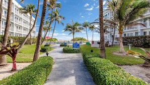 A pathway flanked by palm trees and a building with balconies, leading to a pool area. - Pompano Beach Family Getaway with Pools & Spacious 2BR Retreat (Pompano Beach)