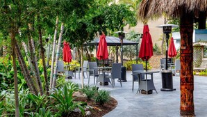 An outdoor patio area with tables and chairs, surrounded by greenery and a thatched structure. - Pompano Beach Family Getaway with Pools & Spacious 2BR Retreat (Pompano Beach)