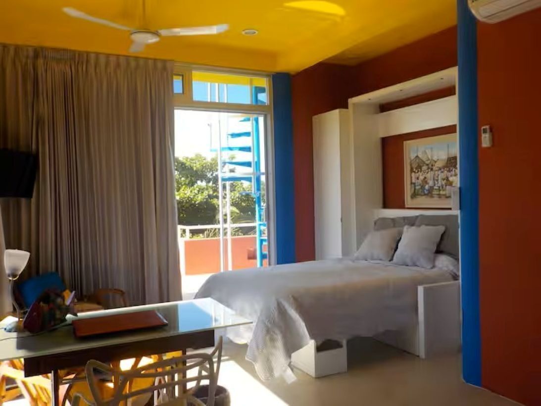 A bedroom with a bed, a desk, a chair, a ceiling fan, and a window with curtains.