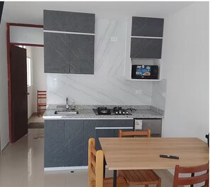 A compact kitchen with dark cabinets, a microwave, a gas stove, and a dining area with a table and chairs. - Private bungalow in Huanchaco (Huanchaco)