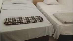 Et værelse med to senge, begge med trægavle, hvide sengetøj og et ternet tæppe på den ene seng.