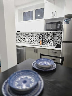 Una cocina con gabinetes blancos, un protector contra salpicaduras con diseño blanco y negro, un microondas y un refrigerador.