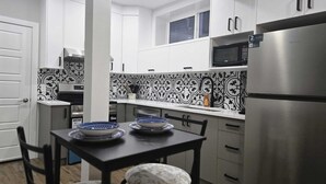 Uma cozinha compacta com armários brancos, uma geladeira de aço inoxidável, um micro-ondas e um painel de fundo padronizado.