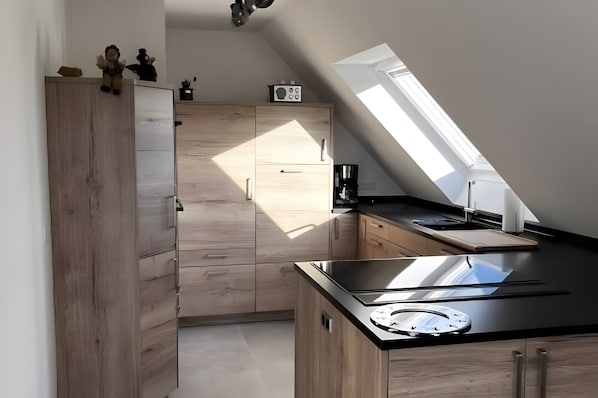A modern kitchen with wooden cabinets, a black countertop, and a skylight.