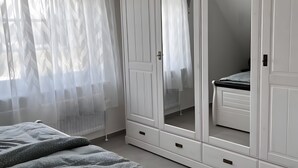 Un dormitorio con cama, armario y ventana con cortinas traslúcidas.