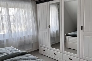 Ein Schlafzimmer mit Bett, Kleiderschrank und einem Fenster mit durchsichtigen Vorhängen.