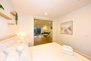 A hotel room with a bed, bedside lamp, a painting, and a view of the dining area. - Contemporary City Stay with Wellness Access (Christchurch)