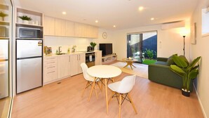 Une cuisine moderne équipée d’un réfrigérateur, d’un four à micro-ondes et d’une cuisinière. On y trouve un coin repas avec une table et des chaises, ainsi qu’un canapé vert dans le salon.