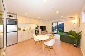 A modern kitchen with a refrigerator, microwave, and stove. There is a dining area with a table and chairs, and a green sofa in the living room. - Contemporary City Stay with Wellness Access (Christchurch)