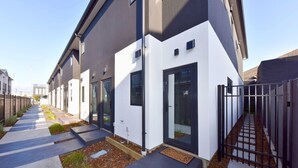 Un immeuble résidentiel moderne au design épuré et géométrique, doté d’une allée étroite et d’une entrée sécurisée par un portail.
