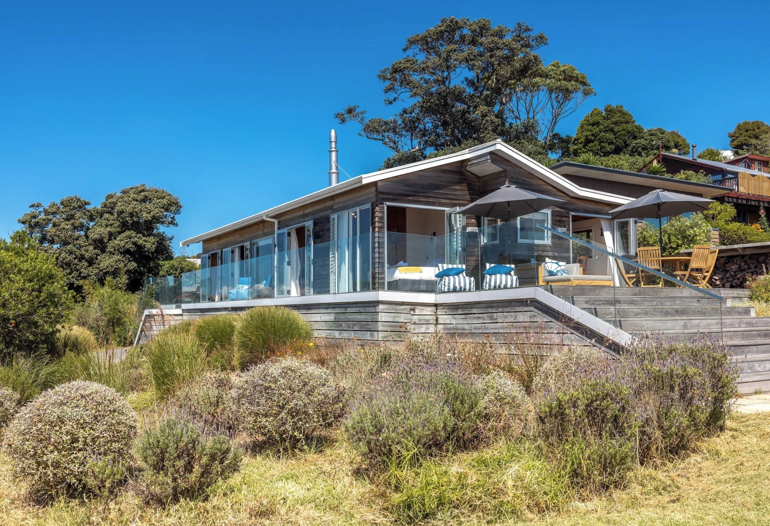 A modern house with a glass facade, a wooden deck, and a staircase leading to the entrance.