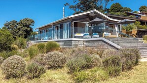 Une maison moderne avec une façade en verre, une terrasse en bois et un escalier menant à l’entrée.