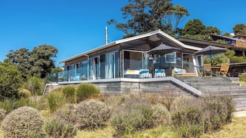 A modern house with a glass facade, a wooden deck, and a staircase leading to the entrance.