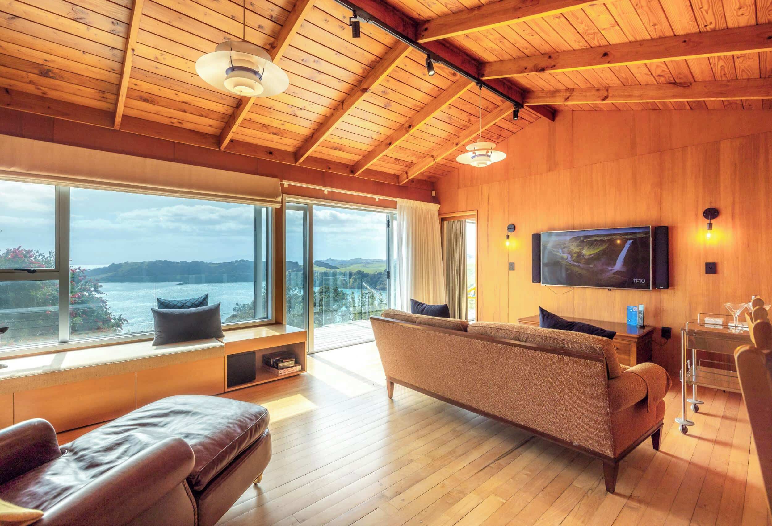 A spacious living room with a large window, a sofa, a television, and a wooden ceiling.