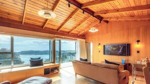 Un salon spacieux avec une grande fenêtre, un canapé, un téléviseur et un plafond en bois.