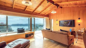A spacious living room with a large window, a sofa, a television, and a wooden ceiling.