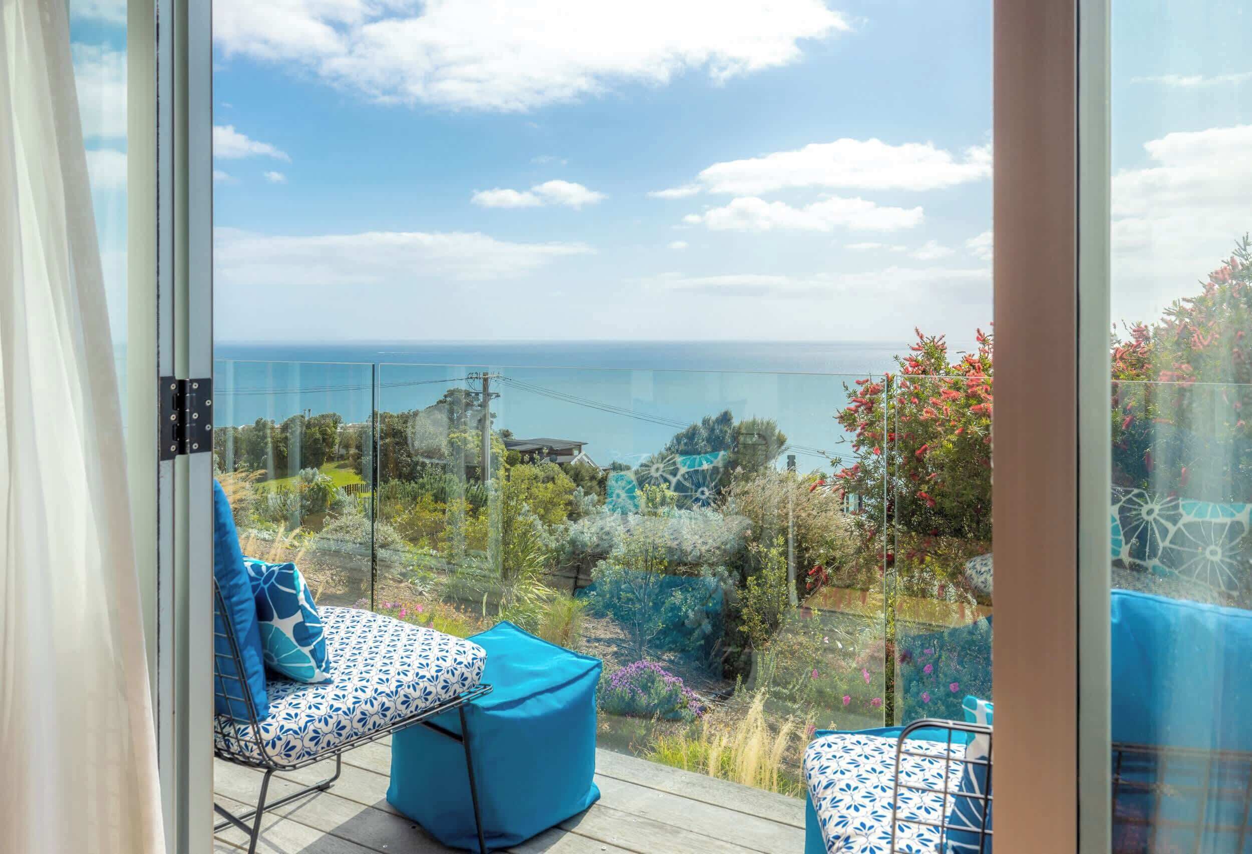 A balcony with a view of the sea, a glass railing, and outdoor furniture.