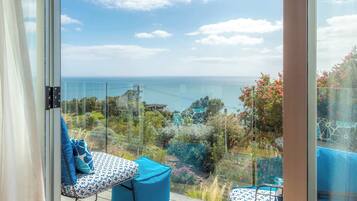A balcony with a view of the sea, a glass railing, and outdoor furniture.
