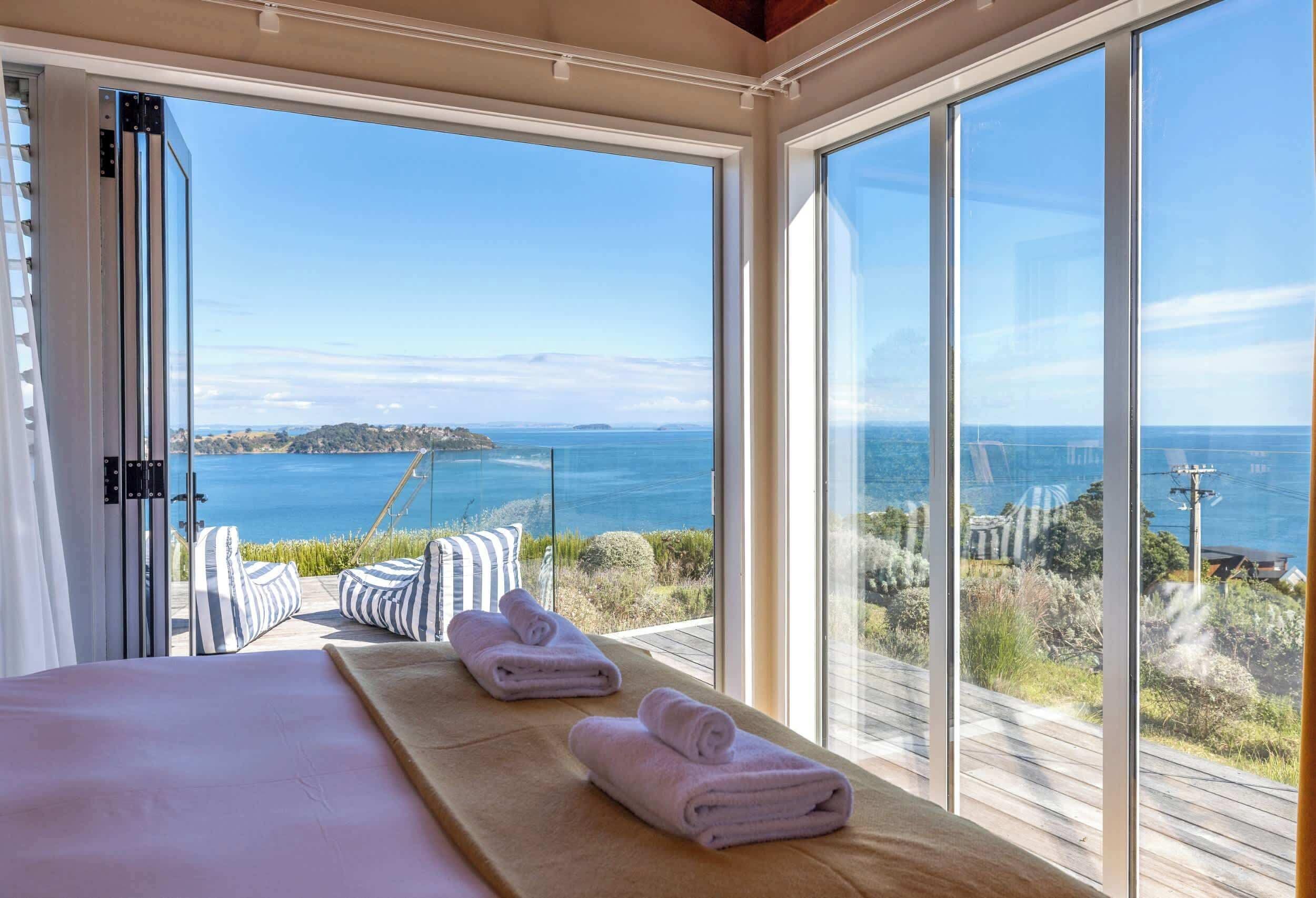 A bedroom with a large window, a bed with pillows, and two towels on a wooden platform.
