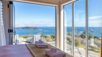 A bedroom with a large window, a bed with pillows, and two towels on a wooden platform.