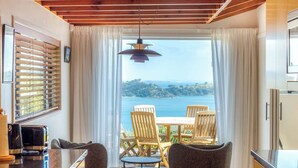 Une pièce avec vue sur la mer, une table avec des chaises, un luminaire suspendu et une fenêtre avec des stores.