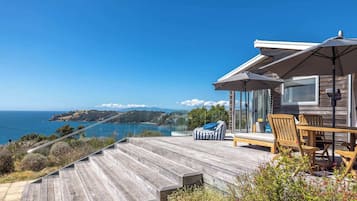 A wooden deck with outdoor furniture, a glass balustrade, and a view of the ocean.