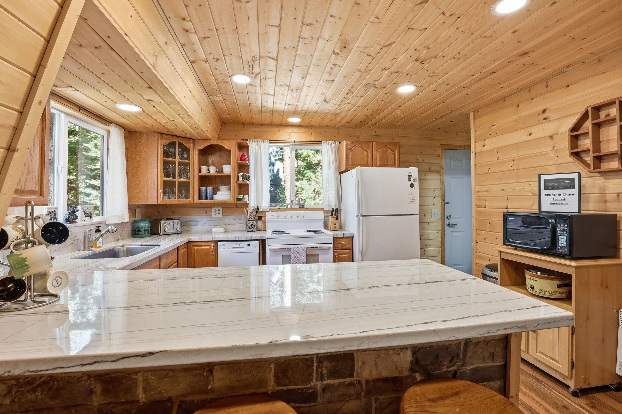 A wooden cabin kitchen with a marble countertop, wooden cabinets, a white refrigerator, and a microwave.