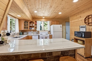 Cocina de una cabaña de madera con encimera de mármol, armarios de madera, un refrigerador blanco y un microondas.