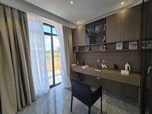 Ein modernes Zimmer mit Schreibtisch, Stuhl und großen Fenstern mit Vorhängen.