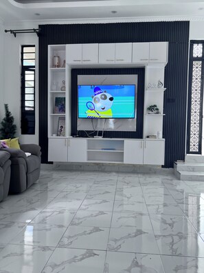 Ein Wohnzimmer mit Flachbildfernseher, grauem Sofa und Marmorboden.
