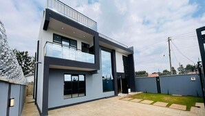 A modern two-story house with a balcony, large windows, and a paved backyard.