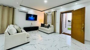 A modern living room with a flat-screen TV, a sofa, a coffee table, and a wooden door.