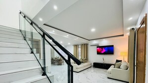 A modern living room with a staircase, a flat-screen TV, and a dining area.